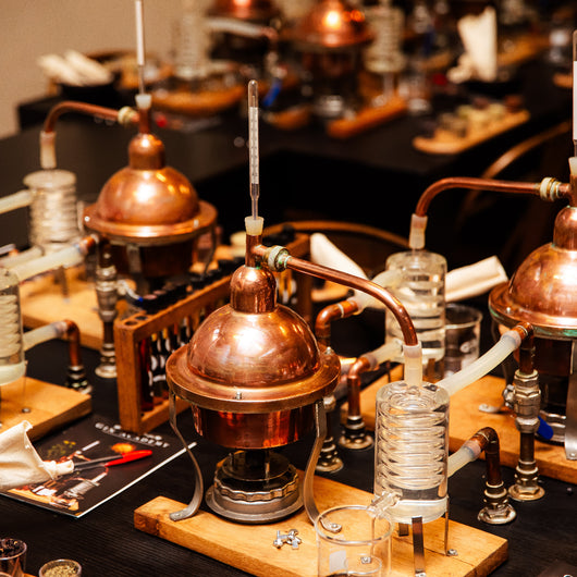 Copper stills and glassware on a table, likely in a distillery setting.